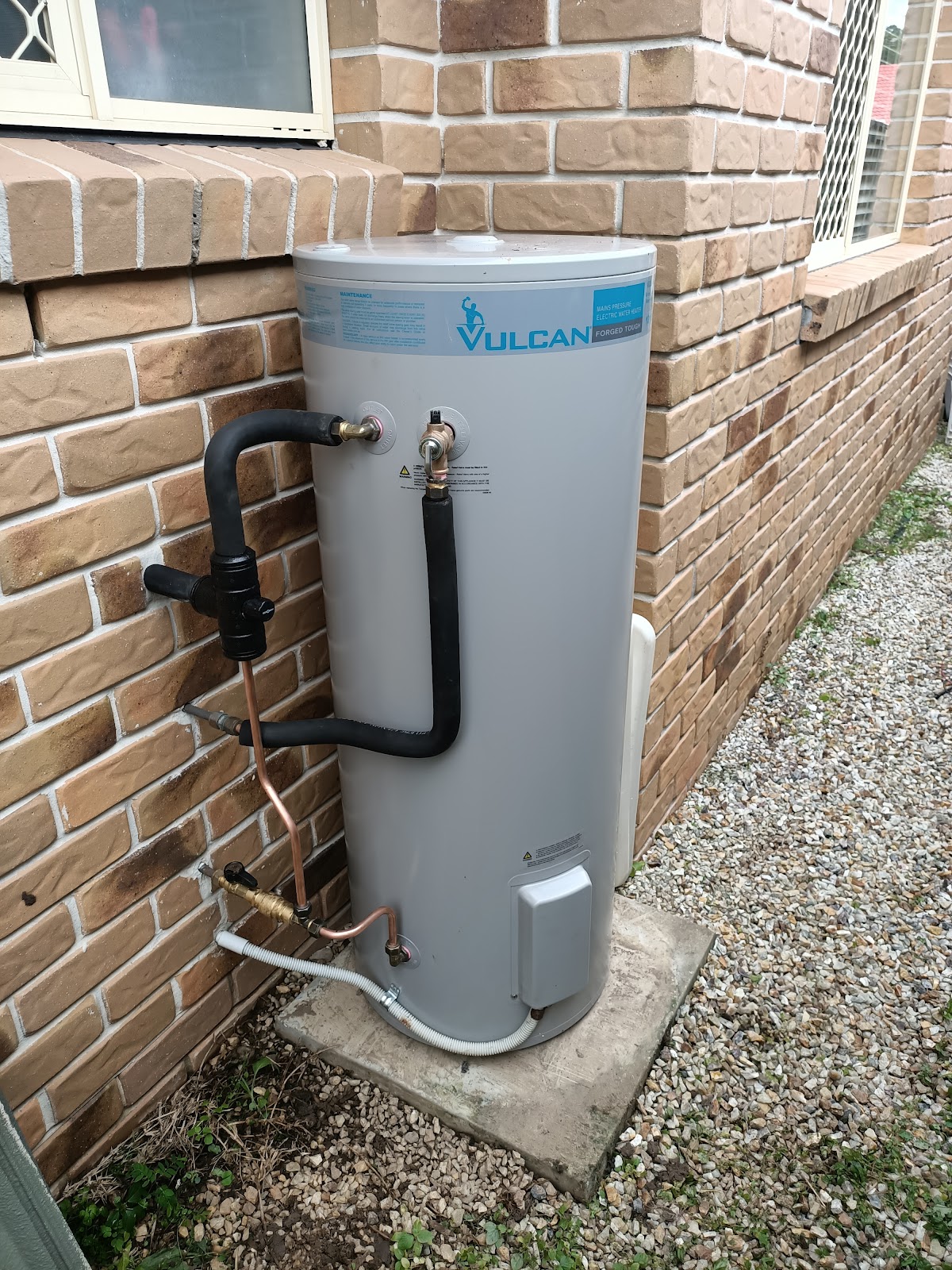 A Vulcan electric hot water cylinder installed on a slab beside a brick house